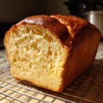 A golden-brown loaf of zero carb yogurt bread cooling on a wire rack, showcasing its fluffy interior.