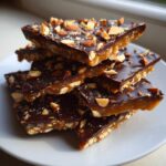 Stack of homemade almond toffee recipe pieces with a thick chocolate layer and chopped nuts.