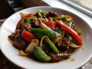 Close-up of savory pepper steak stir-fry with beef, green peppers, red peppers, and onions in a rich sauce.