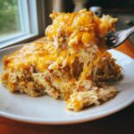 A fork lifts a cheesy, stringy portion of amazing angel chicken rice casserole from a white plate.