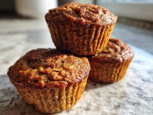 Close-up of three golden-brown, freshly baked bran muffins stacked on a light countertop.