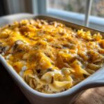 A close-up of a freshly baked Amish country casserole in a white baking dish, topped with melted cheddar cheese and herbs.