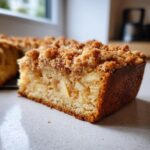 A close-up of a moist slice of apple crumb cake, showing chunks of apple and a golden crumb topping.