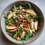 A close-up overhead view of a refreshing apple feta salad with arugula, crumbled feta cheese, walnuts, and apple slices.