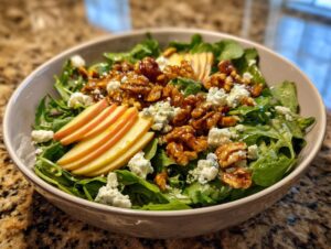A close-up of a vibrant apple feta salad featuring sliced apples, crumbled feta cheese, and glazed walnuts on a bed of greens.