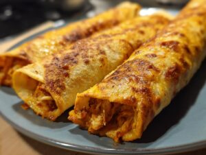 Close-up of golden brown baked chicken taquitos filled with shredded chicken and cheese on a blue plate.