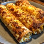 Close-up of three golden-brown baked chicken taquitos with melted cheese on a gray plate.