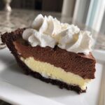 A decadent slice of black bottom pie with chocolate crust, vanilla filling, chocolate mousse, and whipped cream.