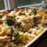 Close-up of a bubbling Broccoli Rice Chicken Casserole topped with melted cheese and visible chunks of chicken and broccoli.