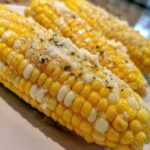 Close-up of three ears of cheesy garlic butter corn on the cob, sprinkled with herbs.