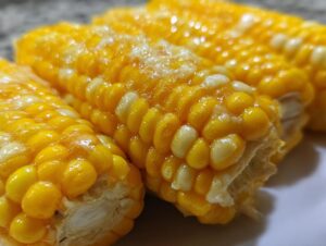 Close-up of delicious cheesy garlic butter corn on the cob, showing kernels glistening with butter.