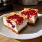 Two delicious Christmas cheesecake bars topped with bright red cherry filling on a white plate.