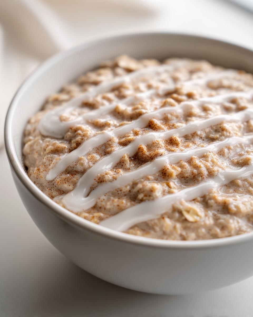 Close-up of creamy overnight oats topped with cinnamon powder and a white icing drizzle.