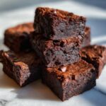 A stack of rich, dark chocolate cottage cheese protein brownie bites, some with chocolate chips visible.
