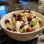 A close-up of a white bowl filled with delicious Cranberry Apple Chicken Salad, featuring shredded chicken, diced celery, and whole cranberries.