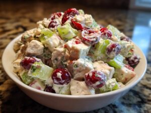 A close-up of a white bowl filled with creamy cranberry apple chicken salad, featuring chunks of chicken, celery, and whole cranberries.