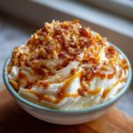 A bowl overflowing with creamy white dip, generously drizzled with caramel and topped with crunchy nuts and caramel pieces, for cream cheese caramel apple dip.