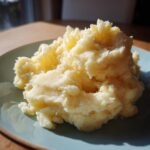 A close-up of a generous serving of creamy, fluffy mashed potatoes on a light blue plate.
