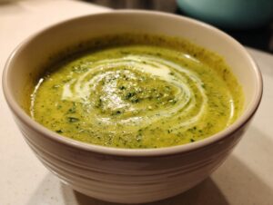 Close-up of a bowl of vibrant green zucchini soup, swirled with cream.