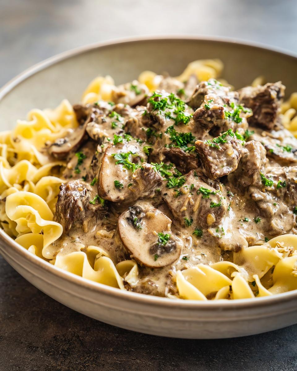 A close-up of Crock Pot Beef Stroganoff served over egg noodles, garnished with fresh parsley.