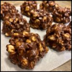 Close-up of several delicious crockpot candy clusters made with chocolate and peanuts, arranged on parchment paper.