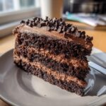 A rich slice of death by chocolate cake with layers of chocolate cake and frosting, topped with chocolate chips.