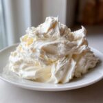 A generous mound of freshly whipped, bright white cream cheese frosting piled high on a white plate.