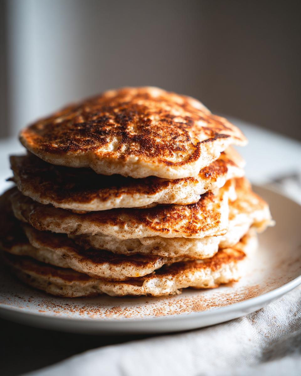 A stack of fluffy pumpkin pancakes dusted with cinnamon on a white plate.