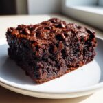 A close-up of a rich, fudgy sweet potato brownie with chocolate chips on a white plate.