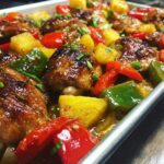 Close-up of glazed chicken thighs mixed with pineapple chunks and colorful bell peppers on a sheet pan for hawaiian chicken sheet pan.