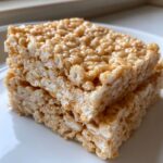 Close-up of two gooey peanut butter rice krispie treats stacked on a white plate.