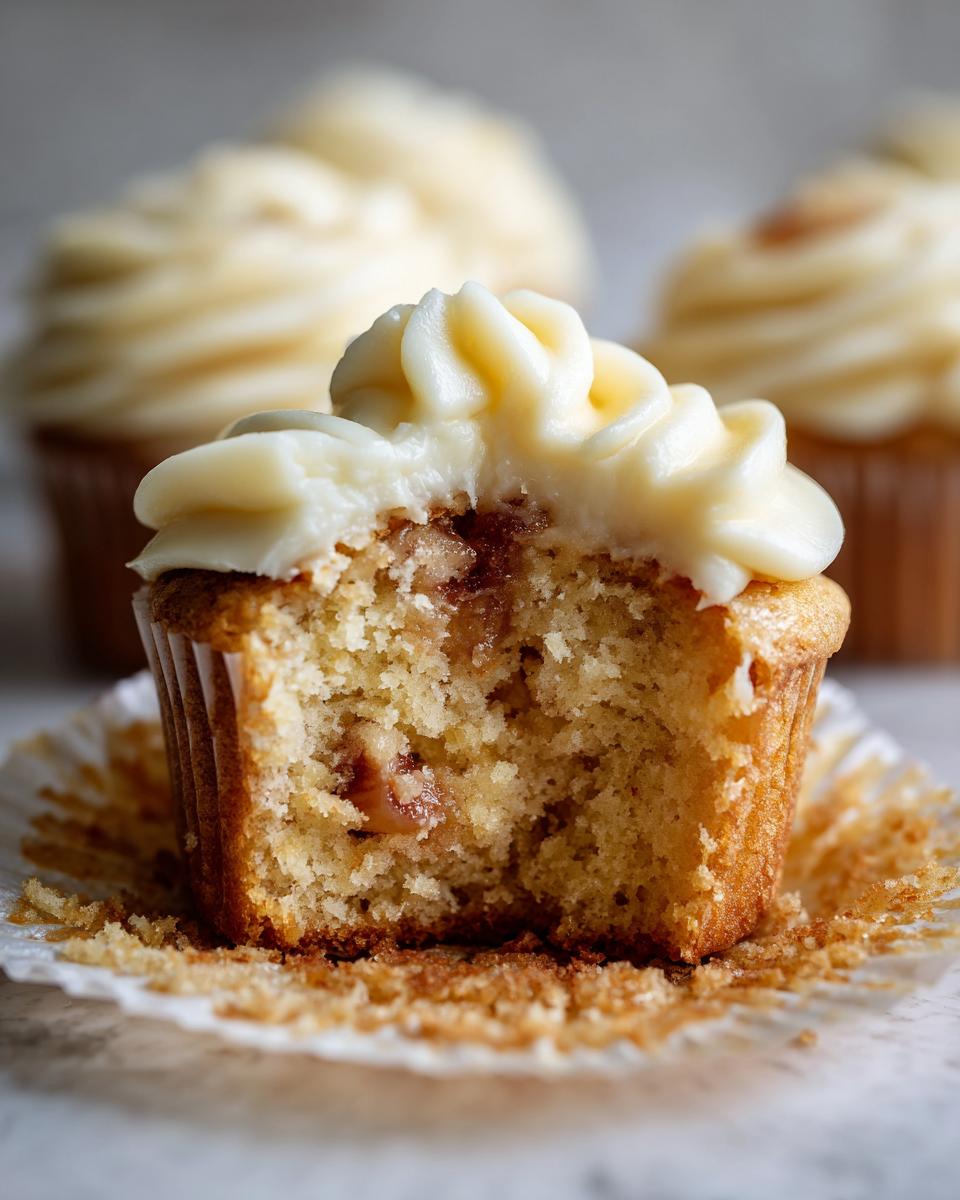 A close-up of a Honey Peach Cream Cheese Cupcake with a bite taken out, revealing the moist interior and creamy frosting.