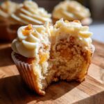 A delicious Honey Peach Cream Cheese Cupcake, cut in half to reveal the peachy filling and fluffy cake.