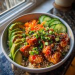 Close-up of a delicious bowl featuring glazed salmon chunks over rice, topped with avocado, carrots, cucumber, and sesame seeds.