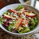 A refreshing honeycrisp apple feta salad with sliced apples, crumbled feta cheese, chopped nuts, and a drizzle of dressing.