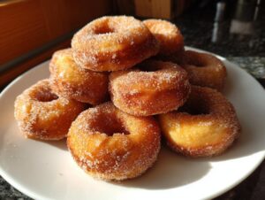 A pile of freshly made hot buttered mini donuts coated in cinnamon sugar on a white plate.