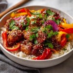 A close-up of a Hot Honey Chicken Bowl filled with rice, glazed chicken pieces, colorful bell peppers, red onion, and cilantro.