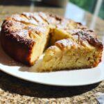 A slice of rustic Italian apple cake (torta di mele) dusted with powdered sugar, showing tender apple pieces within.
