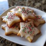 A pile of star-shaped Italian Christmas cookies, generously iced with white glaze and decorated with red and green sprinkles.