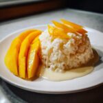 A serving of delicious mango sticky rice with sliced fresh mango and coconut cream sauce.
