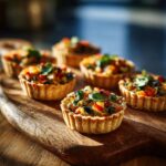 A close-up of several delicious mini vegetable tartlets filled with colorful chopped vegetables and herbs, arranged on a wooden cutting board.
