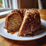 A slice cut from a bundt-style apple cake, generously topped with thick caramel sauce and chopped nuts.