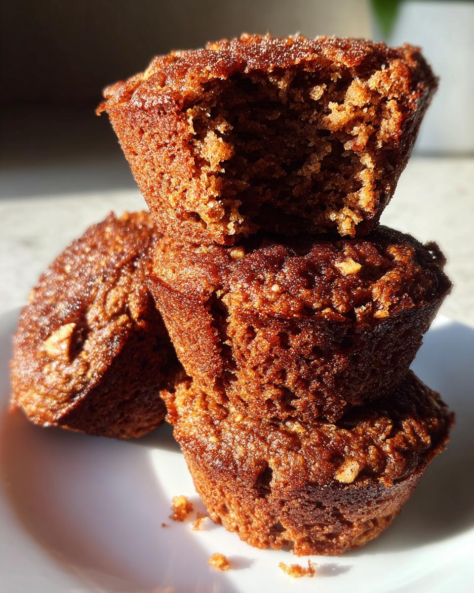 A stack of three moist, dark brown bran muffins, with the top one broken open to show the texture.