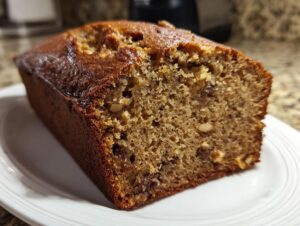 A thick, moist slice of sugar free banana bread featuring a rich brown crust and visible nuts inside.