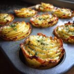 Close-up of baked potato stacks with garlic herb butter in a muffin tin, topped with fresh herbs.