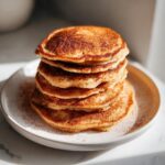 A stack of fluffy pumpkin pancakes dusted with cinnamon on a white plate.