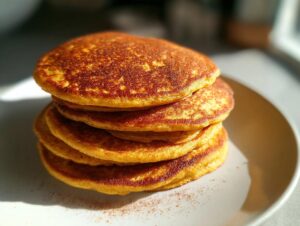 A stack of fluffy pumpkin pancakes dusted with cinnamon on a white plate.