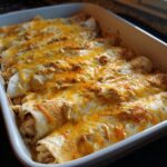 Close-up of baked queso chicken enchiladas in a white baking dish, topped with melted golden cheese.