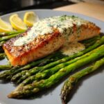 A perfectly cooked salmon fillet topped with creamy dill sauce, served over roasted asparagus spears. A healthy anti-inflammatory dinner.