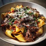 A close-up of a bowl of pappardelle pasta topped generously with rich short rib ragu and grated Parmesan cheese.